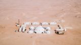 White round tents and containers in a red sand desert arranged in a rectangle. They form the basecamp for the 2018 Mars analog mission in Oman called AMADEE-18.